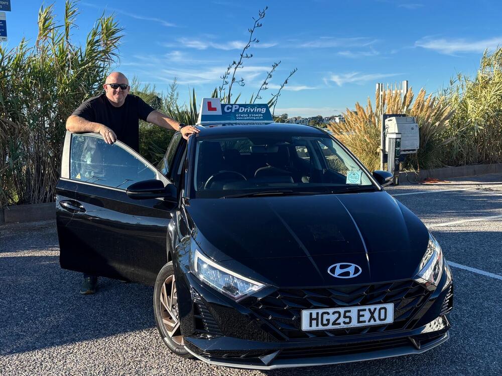 Clinton standing at the open door of his black 2025 Hyundai i20, CP Driving board on the roof