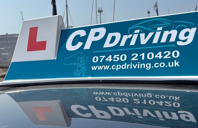 Close-up of the CP Driving roof board showing the L-plate, the phone number 07450 210420 and cpdriving.co.uk