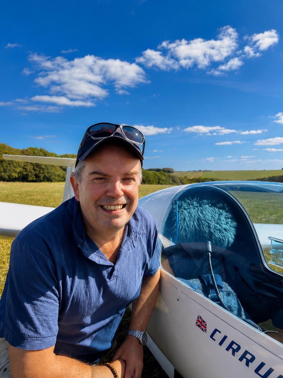 Ian Simmonds, DVSA Approved driving instructor, smiling beside a glider on a sunny airfield